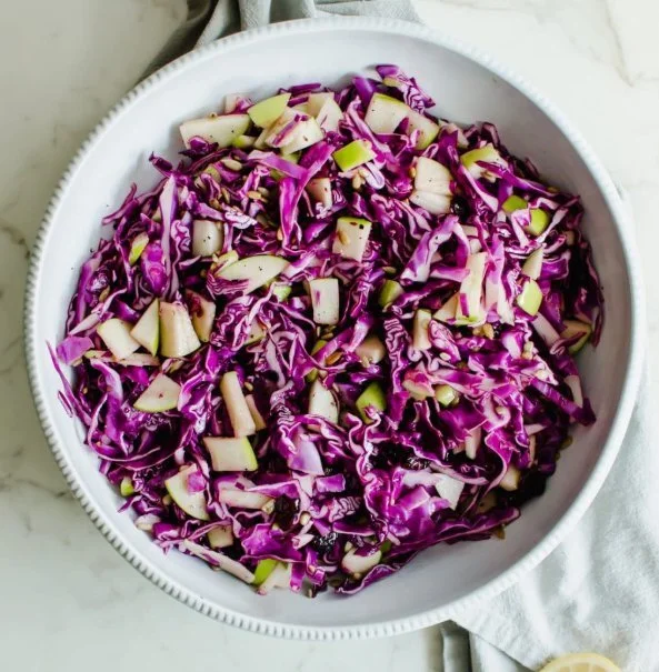 Crispy red cabbage and apple slaw in a bowl with a fresh garnish