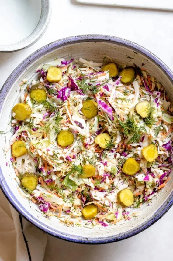 Bowl of spicy dill pickle coleslaw garnished with pickles and herbs