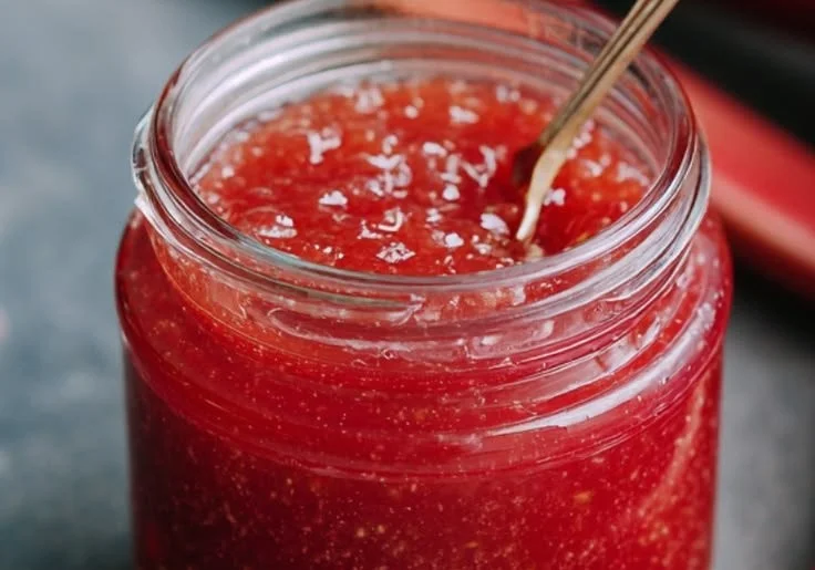 Homemade rhubarb sauce in a bowl with fresh rhubarb stalks