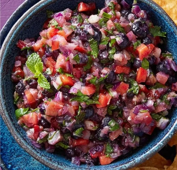 A bowl of jammy blueberry salsa with fresh blueberries and herbs on a rustic table.