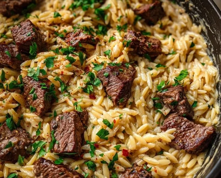 Creamy garlic butter steak orzo dish topped with fresh herbs